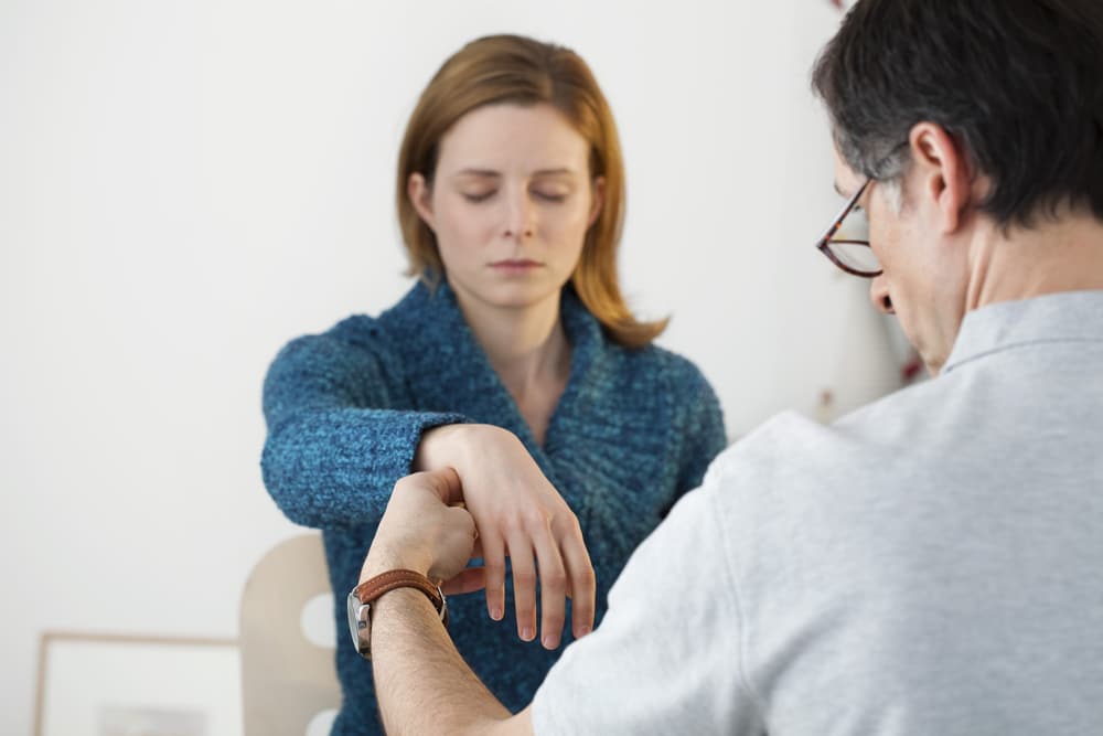 hypnosis testing suggestibility man in grey holding a woman in blue's wrist 