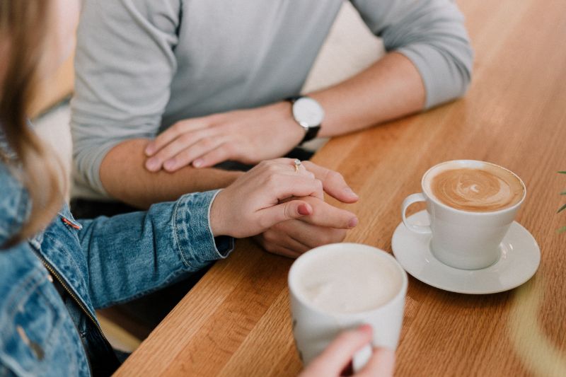 Two hypnotherapists, one female in denim and one male in a grey top; both with hot drinks