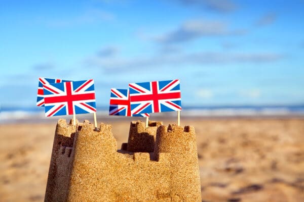 Seasonal marketing image of a sandcastle at the beach with british flags on the turrets.