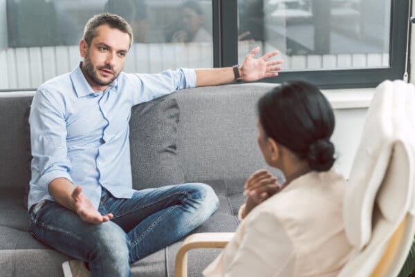 Couple sat talking about a problem, man getting animated and emotional
