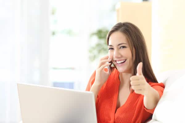 Hypnotherapist on the phone to a client, with her thumb up, smiling.